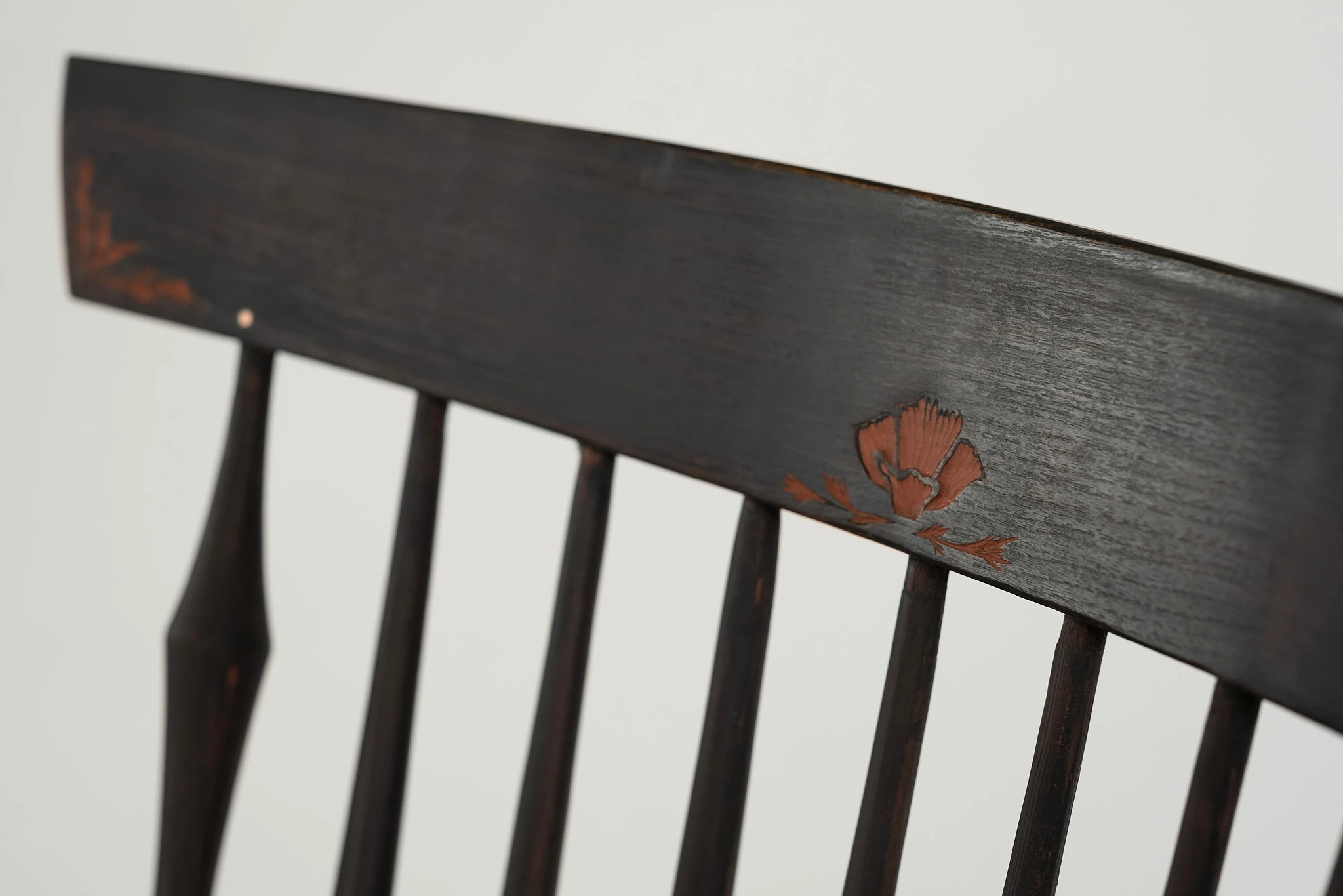 Close up of red-filled carving on the back of a black Windsor chair